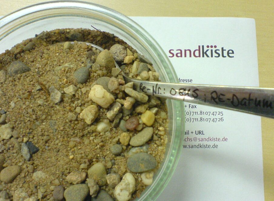 Rechnung der Satzkiste ist zu sehen, neben einer Schale mit Sand und einem Esslöffel mit einer Rechnungs-Nummer